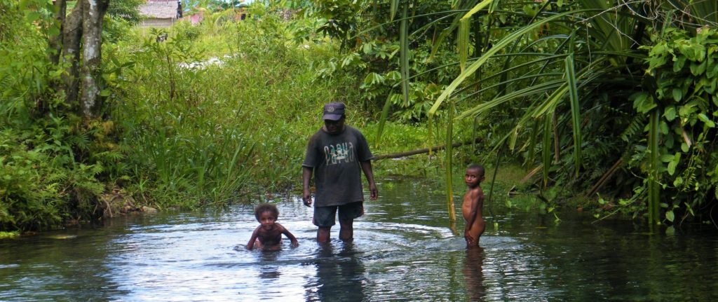 Papuan man with two kids in a river in West Papua while exploring Sorong and surroundings