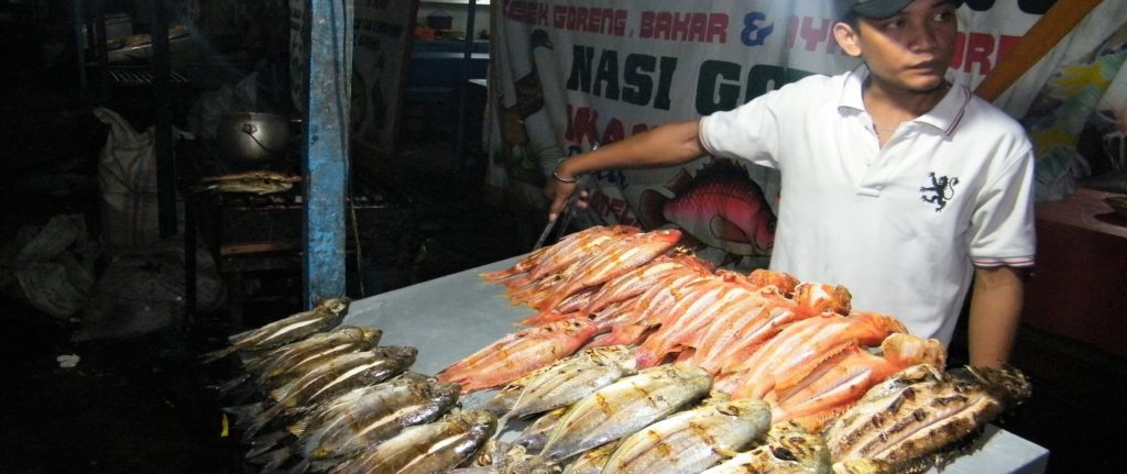 Young man selling grilled fish at Tembok Berlin - best place to eat in Sorong